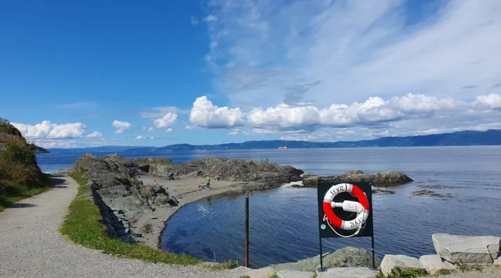 Foto av sandstrand ved fjorden med redningsbøye i forkant