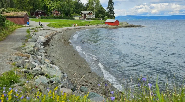 Foto av strand og sti med bygninger i bakgrunnen