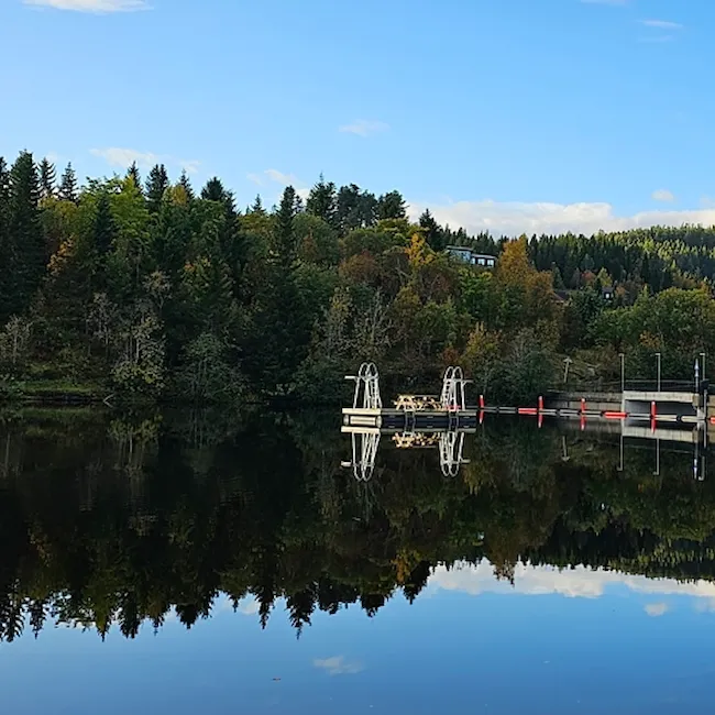 Foto av badebrygge på Theisendammen med demning i bakgrunnen