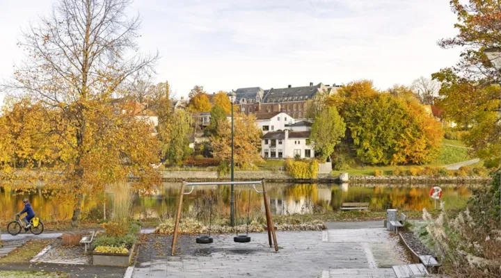 Park med benk og dissestativ. Løv på bakken