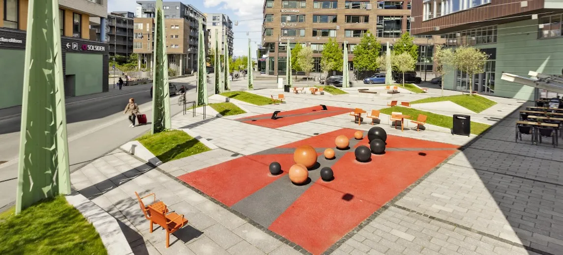Benker og balanse-apparat på en plass med betongheller mellom høye bygg.