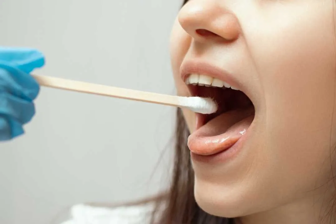 Bilde av en testpinne på vei inn i munnen til en kvinne.