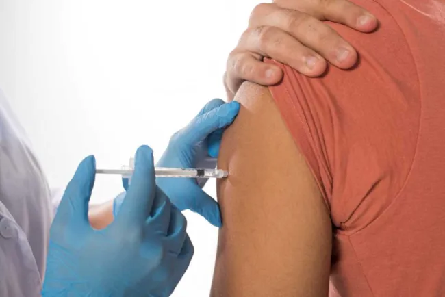 Helseansatt med hansker vaksinerer en person (nærbilde av arm og hender)