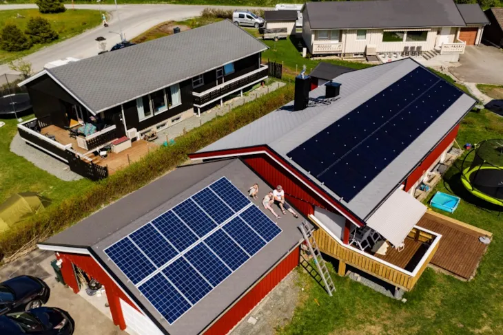 Bilde tatt ovenfra av flere bolighus. P&aring; huset med solceller p&aring; taket sitter en pappa og to barn.