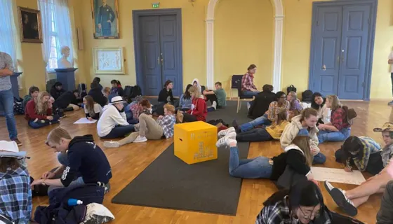 Bilde av vgs-elever som sitter rundt på gulvet og løser oppgaver. Midt i blant dem ser vi en gul kloss med bærekraftsmål 11 på.