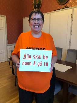 Rita Ottervik som holder opp et ark med teksten alle skal ha noen å gå til