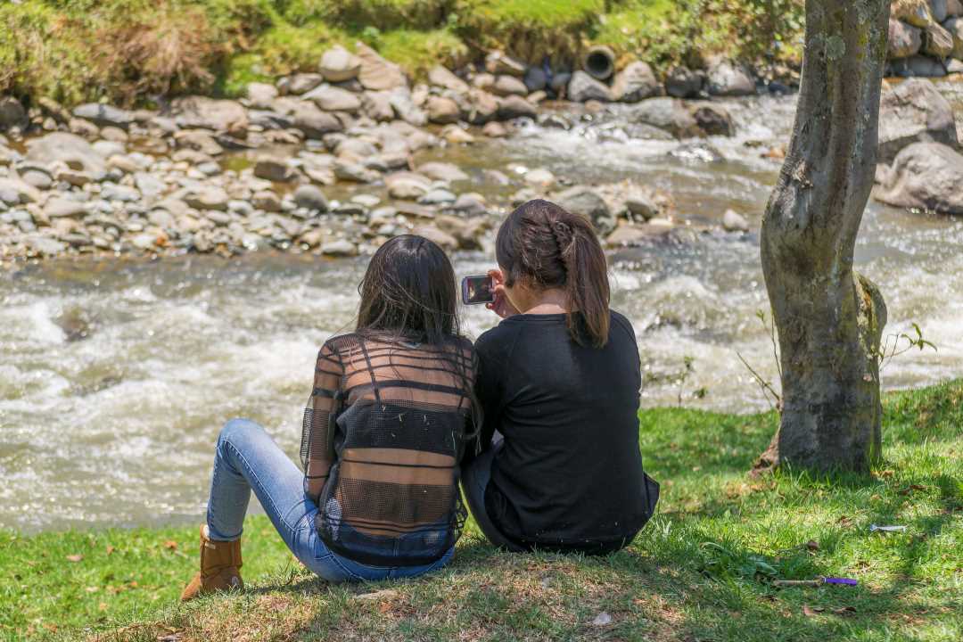 To unge jenter som sitter ved ei lita elv. Bildet skal illustrere tankefull ungdom.