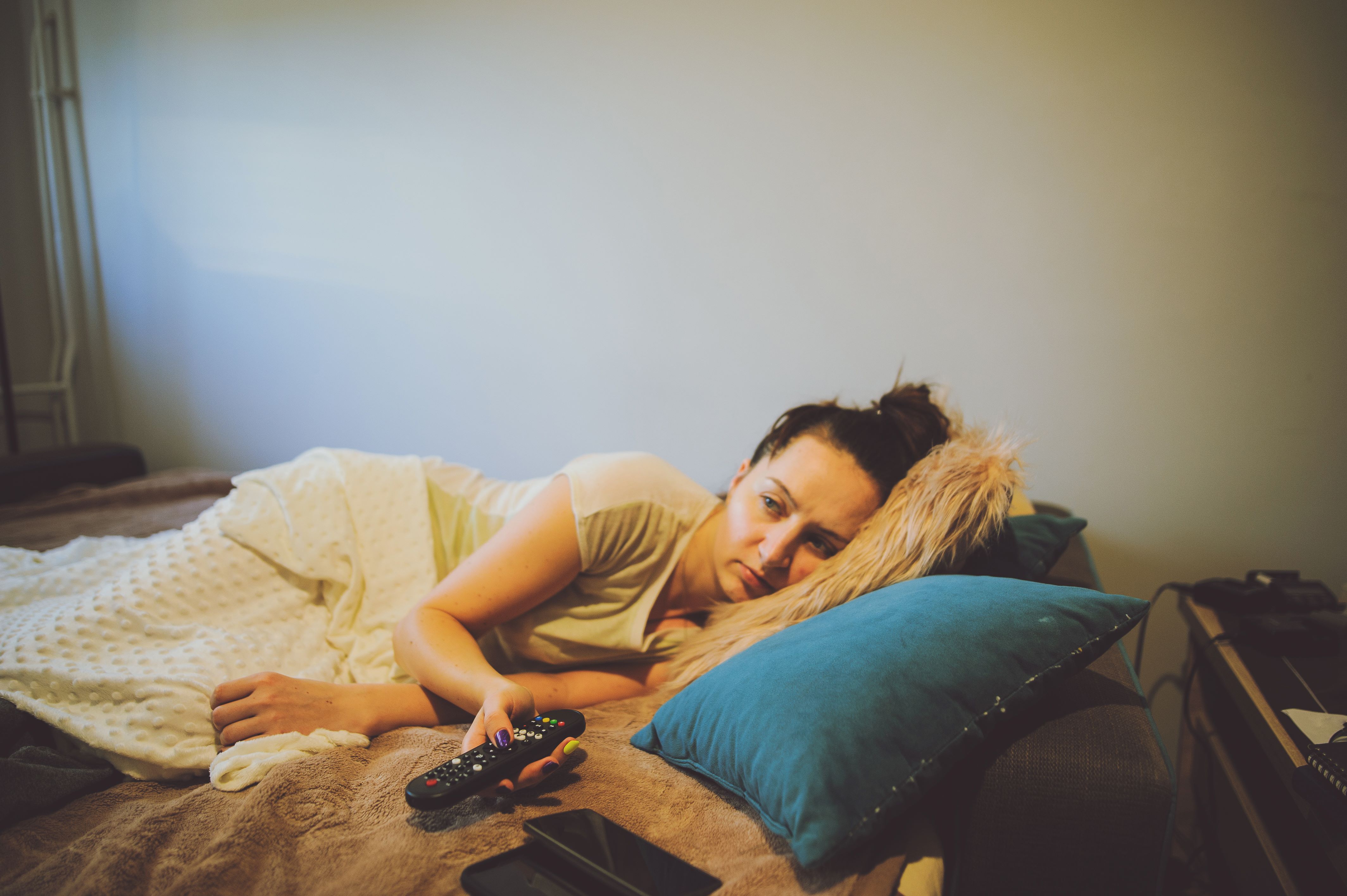 Kvinne som er syk og ligger i senga og trykker på en fjernkontroll.