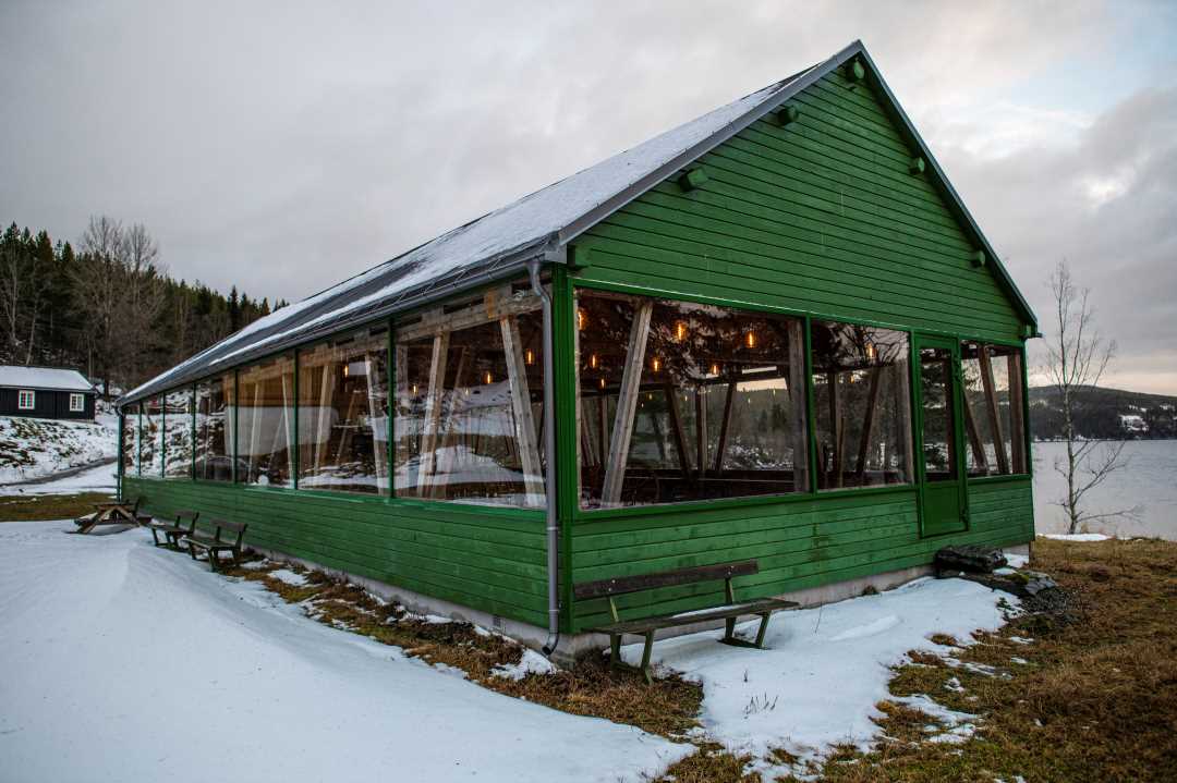 Foto av det grønne samfunnshuset på Teigen, oppført hovedsakelig i tre og med store vindusflater. Den ligger fint til ved Selbusjøen.