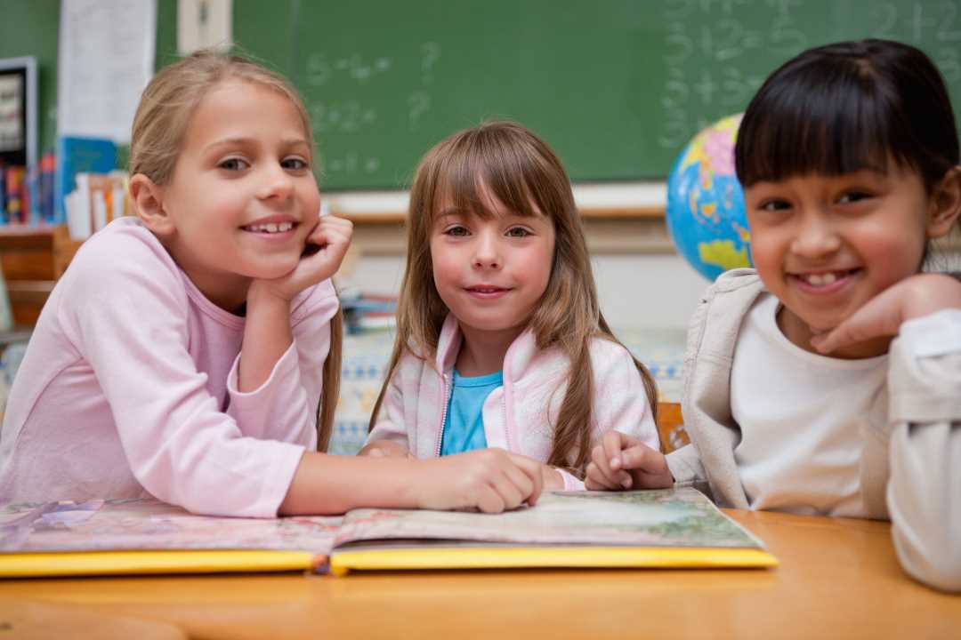 Bilde av tre skoleelever som leser i ei bok