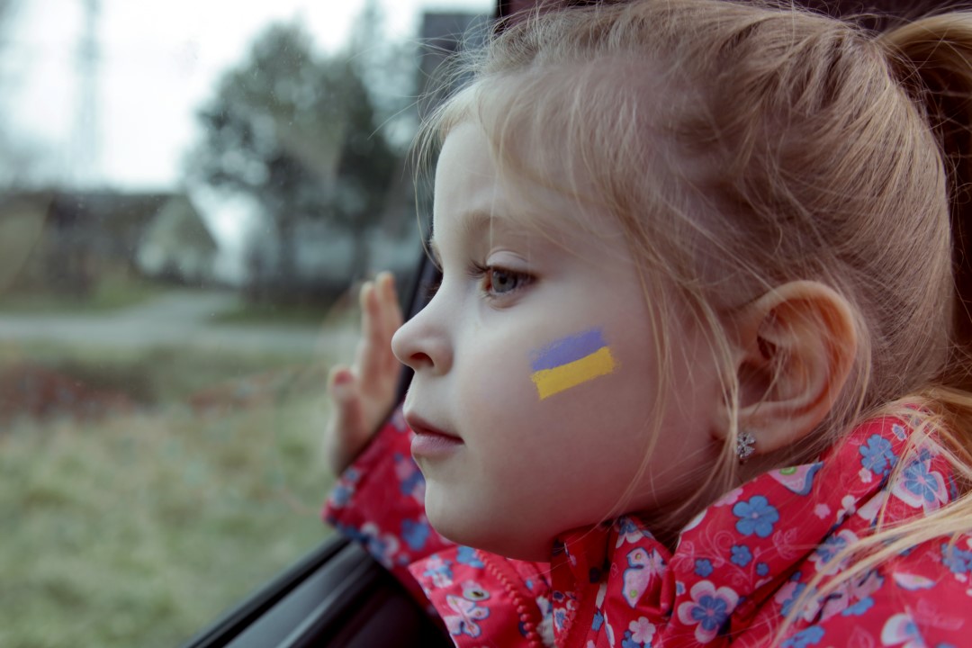 Jente som ser ut av vinduet i et kjøretøy. Hun har det ukrainske flagget malt på kinnet.