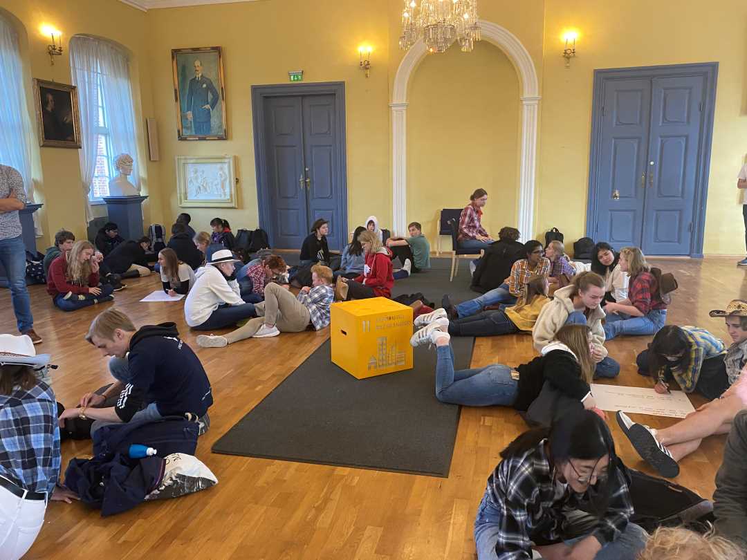 Bilde av vgs-elever som sitter rundt på gulvet og løser oppgaver. Midt i blant dem ser vi en gul kloss med bærekraftsmål 11 på.